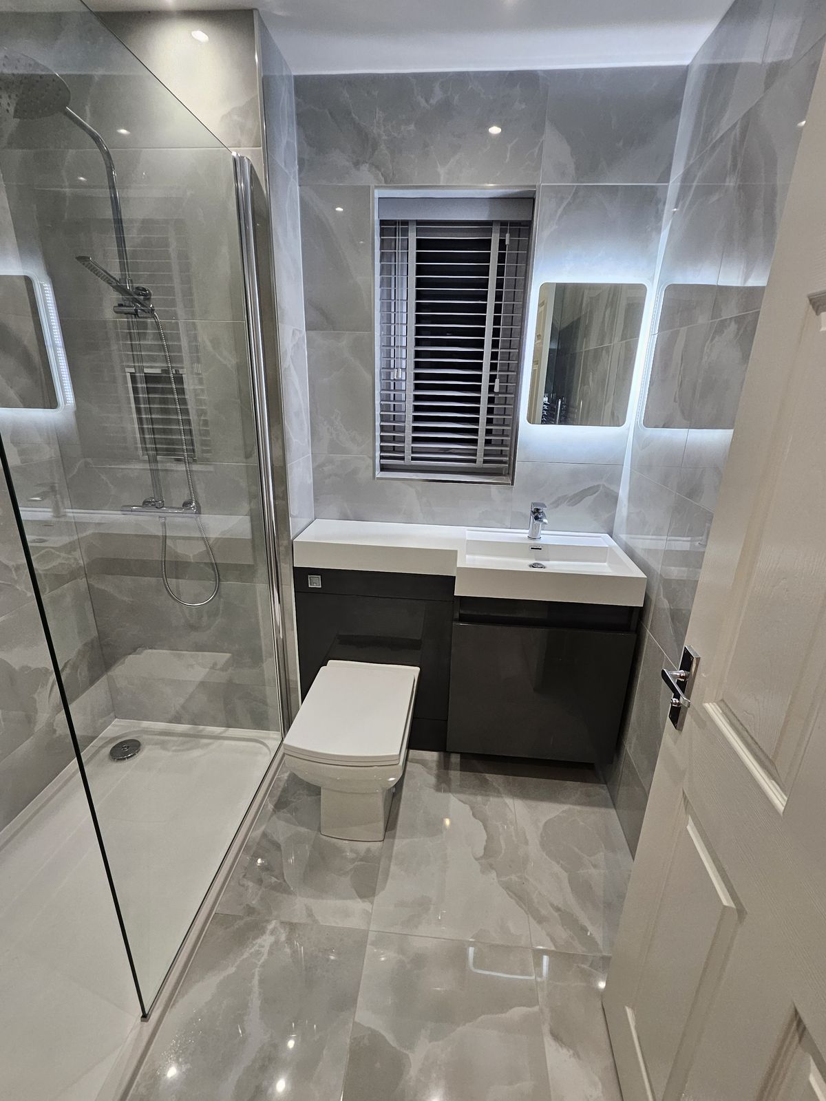 A shower room in grey marble-effect tiles with a grey vanity unit and LED mirrors