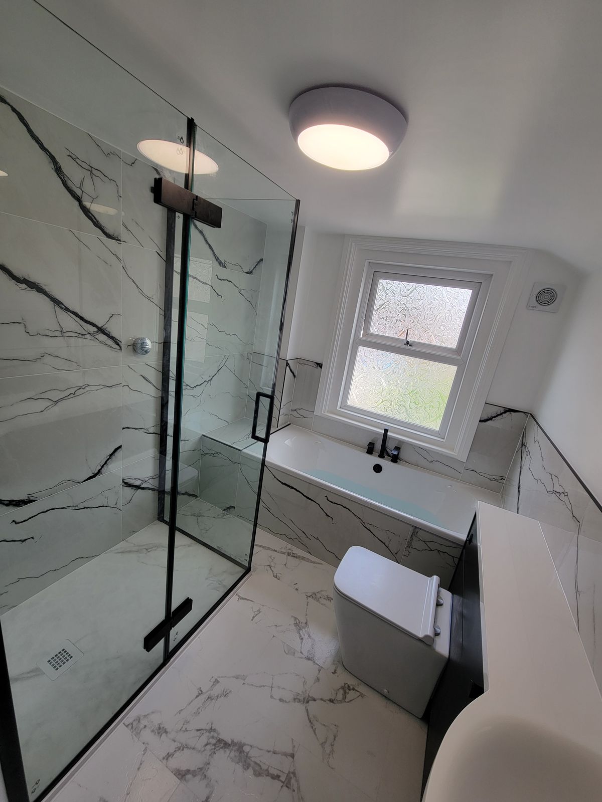 A finished bathroom with white marble-effect tiles, a black-framed walk-in shower and a white basin unit
