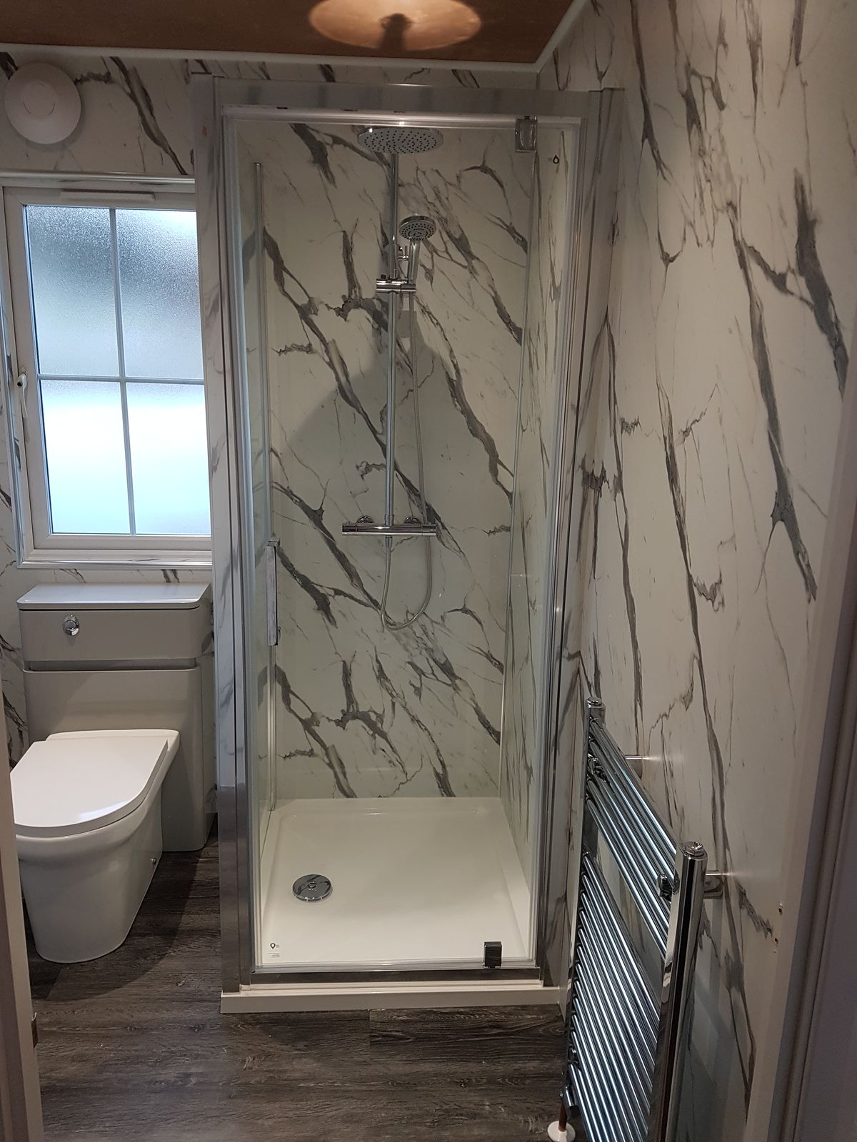 A shower cubicle and towel radiator in a room of white marble-effect panels